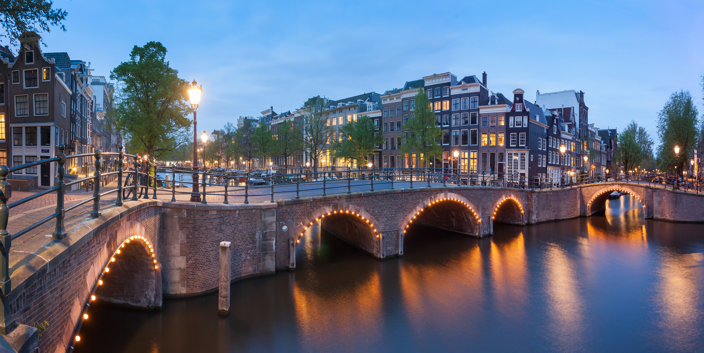 Arched Amsterdam canal bridge outlined in lights at twilight