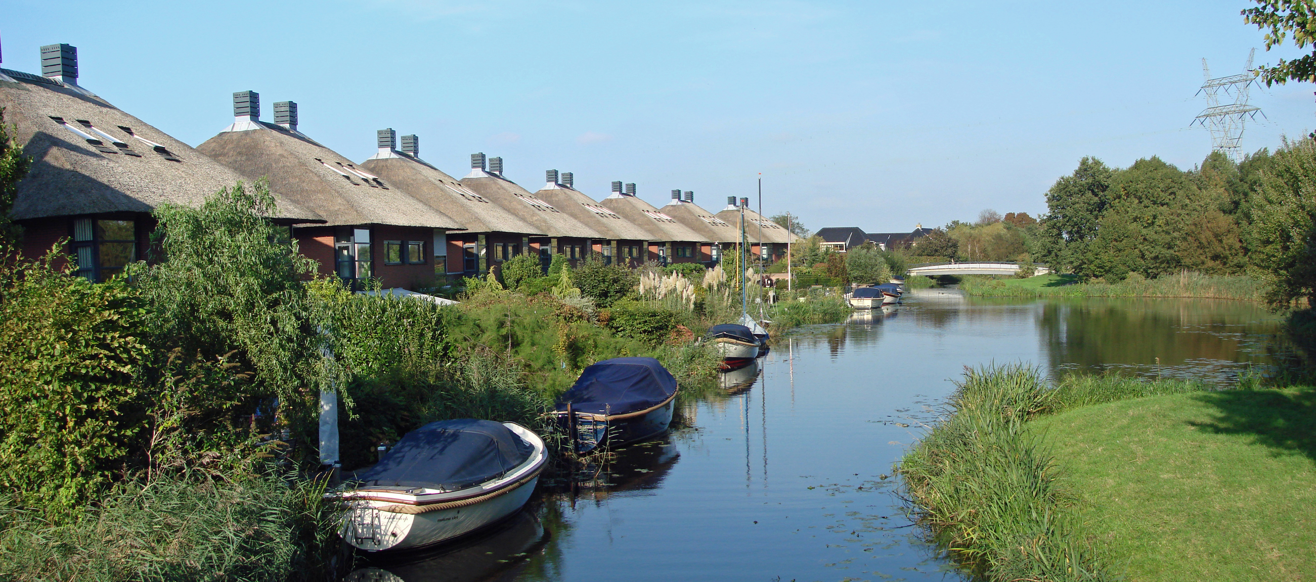 Row of thatched-roof houses beside a quiet Dutch waterway with small moored boats