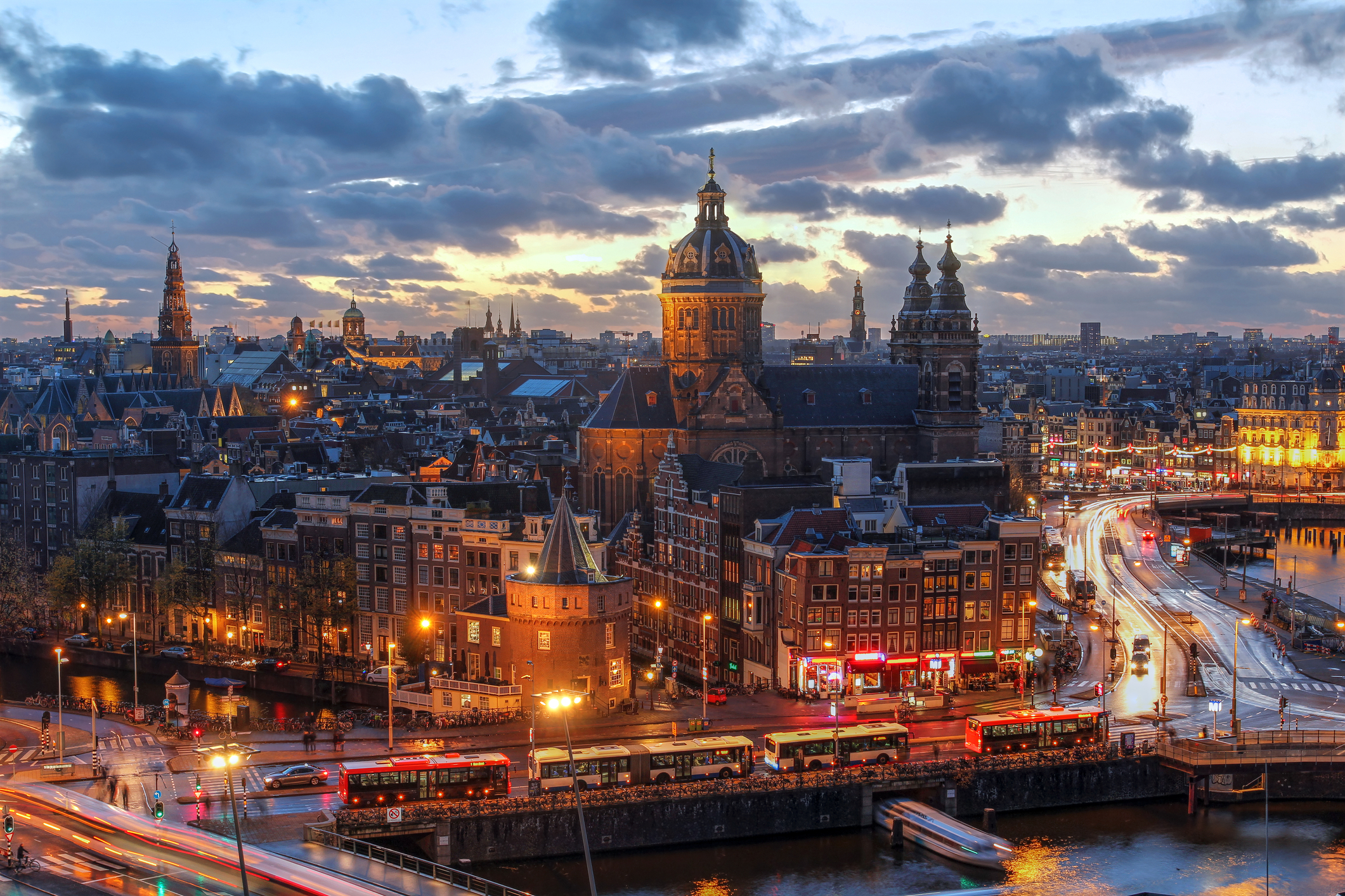 Old Amsterdam rooftops and domed church towers at dusk under a cloudy sky